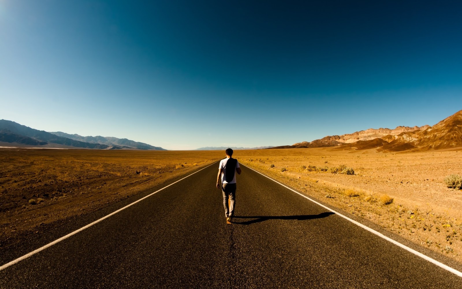 uomo che passeggia su una strada in mezzo ad un deserto con montagne